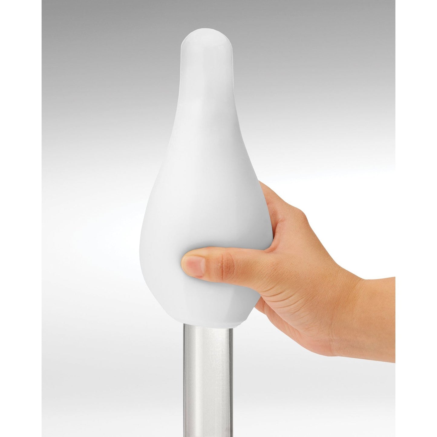 A hand holds a Tenga GEO Glacier - White by Tenga, featuring a teardrop shape and smooth, stretchable material, atop a metallic pole against a gray gradient. Its ergonomic design is both sleek and reusable for practical use.