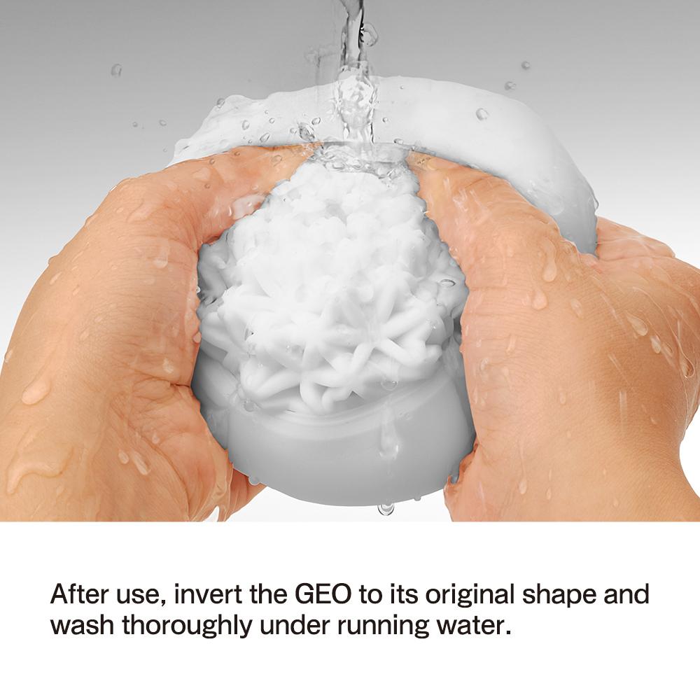Washing the Tenga GEO Glacier - White, a textured round object by Tenga made of stretchable material, under running water. Squeeze it between fingers for a thorough clean. Invert to original shape after use and wash thoroughly under running water for reusable freshness.