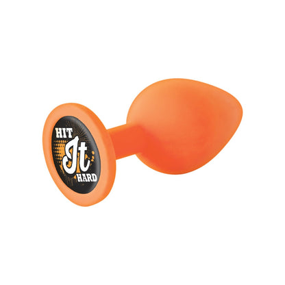 The 9s Booty Calls Hit It Hard Plug is an orange, teardrop-shaped silicone toy with a suction base. It has a phthalate-free design featuring bold white and orange Hit It Hard text on a black and orange patterned background.