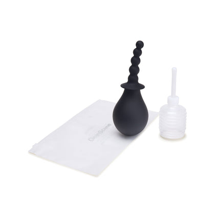 The CleanScene 4 Pc Soft Squeeze Beaded Anal Douche Set With Flared Base, including black silicone anal beads and a travel-friendly clear plastic enema bottle with nozzle, is neatly displayed on a white surface next to a folded white pouch.