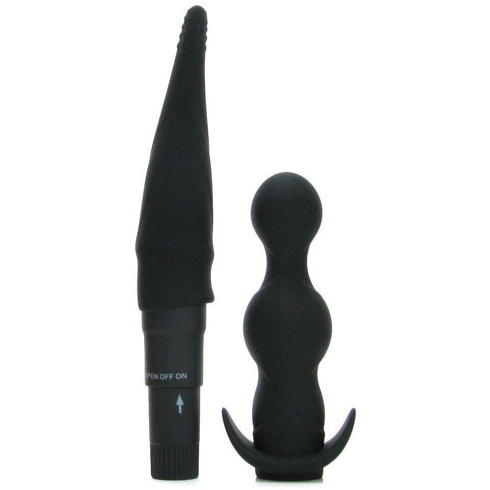 In the Pipedream Anal Fantasy Collection Anal Adventure Kit, two black silicone anal toys stand upright against a white background: on the left, a tapered unisex vibrator with ribbed texture and an on/off switch at the base; on the right, a beaded mini-vibe with a curved base for easy handling.