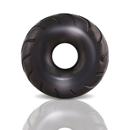 A glossy, black, donut-shaped object made from stretchy X5Plus material with subtle grooves and a central hole resembles the Blush Performance Truck Tire Cock Ring by Blush Novelties. Its shown on a plain white background with a soft reflection beneath.