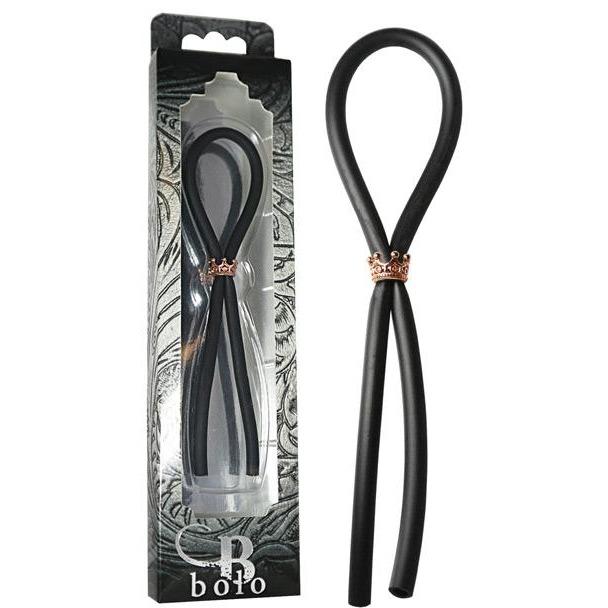 Adams Toy Box presents the Bolo Silicone Lasso with a rose gold crown slider ring, neatly displayed in decorative packaging with black and gray abstract designs. A clear window reveals the elegant black silicone tie crafted from body-safe materials.