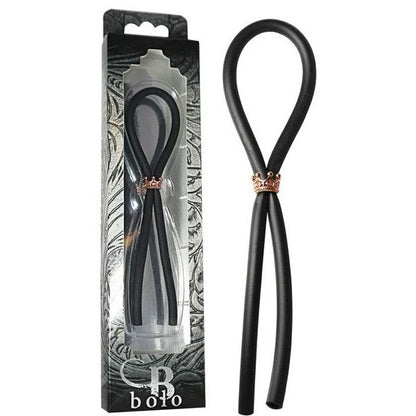 Adams Toy Box presents the Bolo Silicone Lasso with a rose gold crown slider ring, neatly displayed in decorative packaging with black and gray abstract designs. A clear window reveals the elegant black silicone tie crafted from body-safe materials.
