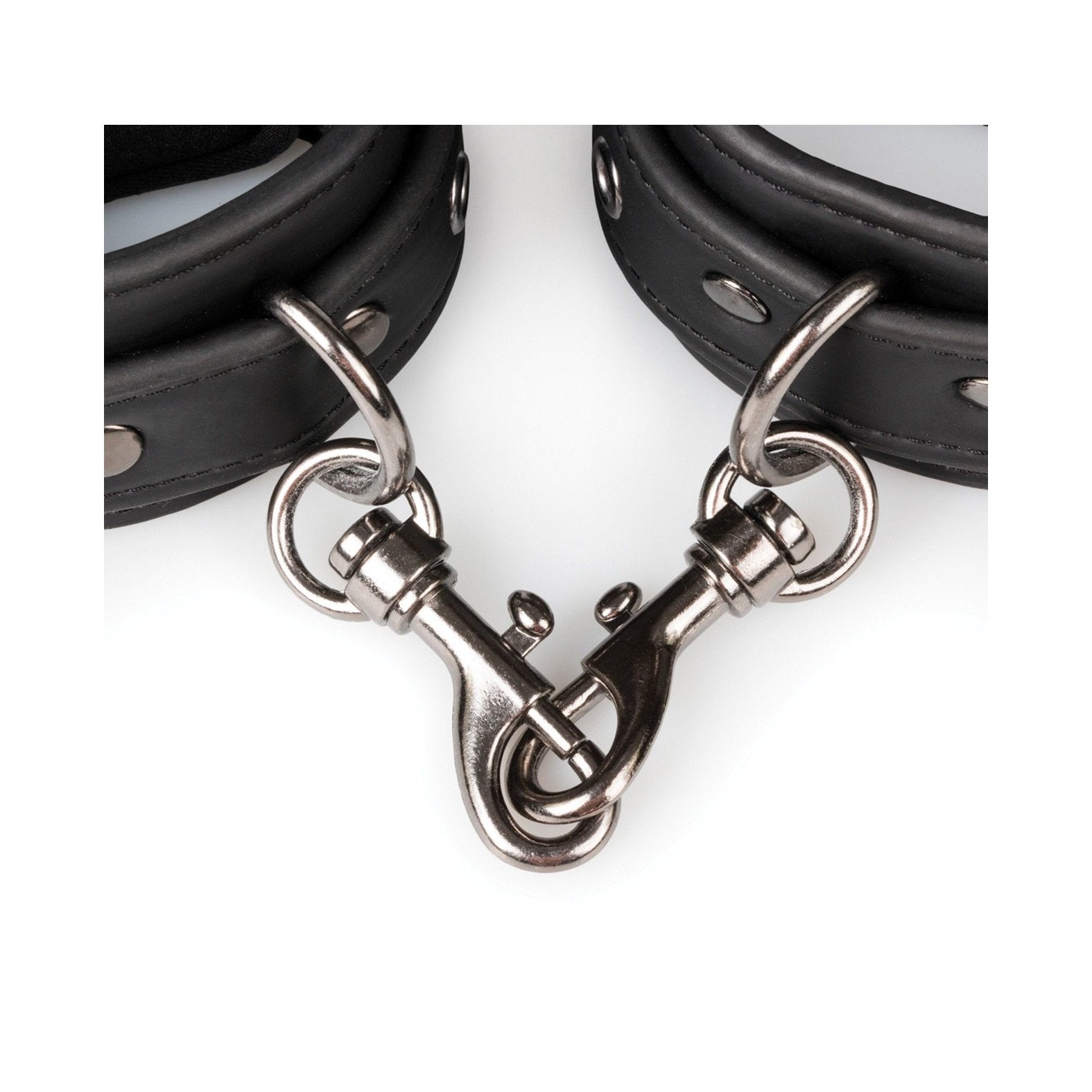 A close-up of Easy Toys Faux Leather Handcuffs reveals two interconnected black leather cuffs. These adjustable restraints from Easy Toys come with metal studs, a swivel clasp, and D-rings for secure attachment.