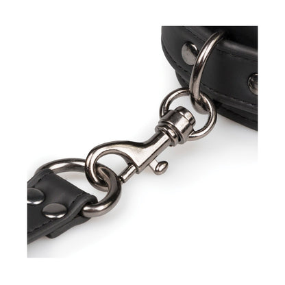 A close-up of the Easy Toys Faux Leather Hogtie shows a shiny silver swivel snap hook attached to a black faux leather strap, featuring metal studs and stitching. The loop connects it elegantly to a thicker strap, ideal for restraint setups.