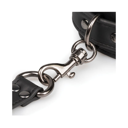 A close-up of a metal clasp connects two black leather straps with rivets, typical of durable fasteners in bondage gear. These straps could be part of the Easy Toys Hogtie with Hand & Ankle Cuffs by Easy Toys, featuring an adjustable cuff set.