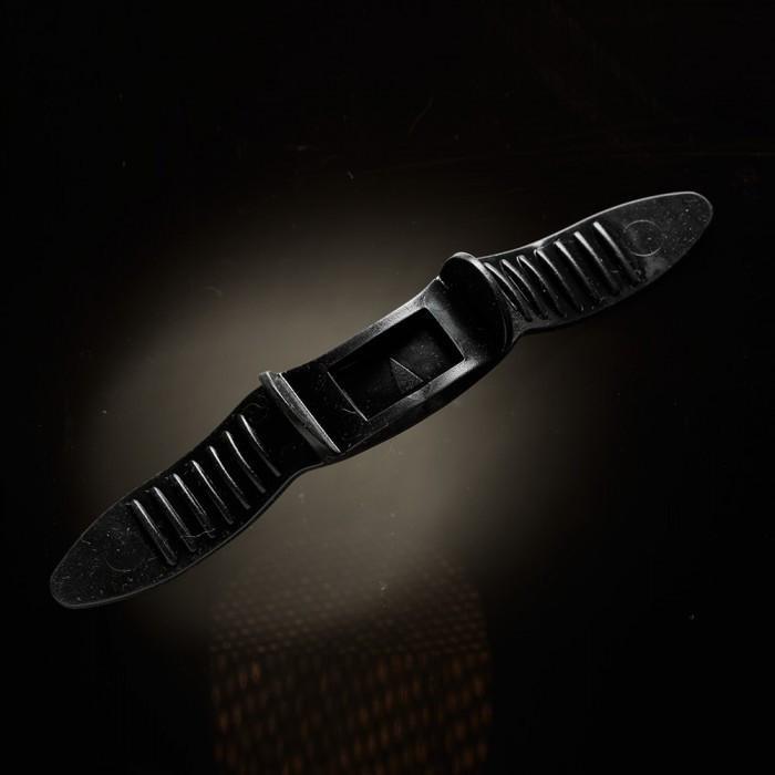 A dark rectangular object with ribbed handles is set against a blurred, illuminated background. It resembles the Male Edge Pro Penis Enlarger Kit by Male Edge, showcasing a small central opening and textured surfaces that may incorporate traction technology for improved usability.