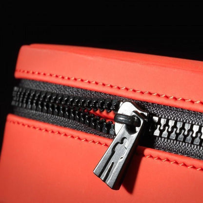 Close-up of a black zipper on an orange Male Edge Pro Penis Enlarger Kit bag, captured at an angle with dramatic lighting highlighting the textures. The zipper pull prominently displays a distinctive silhouette design on its metal surface.