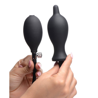 Two hands hold a Master Series Dark Inflator, an inflatable silicone anal plug designed for stretching pleasure. On the right, the plug connects to a bulb pump with release valve on the left. The background is plain white.