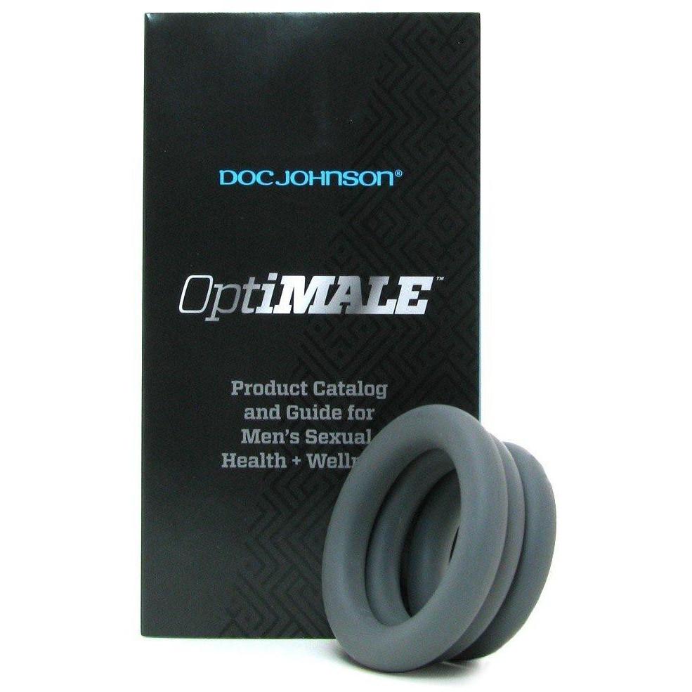 A black product box features OptiMale C Ring Kit Thick and Product Catalog and Guide for Mens Sexual Health + Wellness in white text. In front are two super stretchy silicone rings for long-lasting erections. The top blue text reads Adams Toy Box.