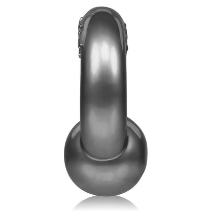 The Oxballs Gauge Cockring, exhibiting a sleek and curved design with a dark metallic SuperFLEXtpr finish, rests against a white background.