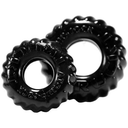 The Oxballs TruckT Cock & Ball Ring pack features two black, tire-shaped dog chew toys with knobby texture, crafted from durable Skinflex TPR. Their shiny surface and embossed text add toughness. One toy is larger to suit different dog breeds.