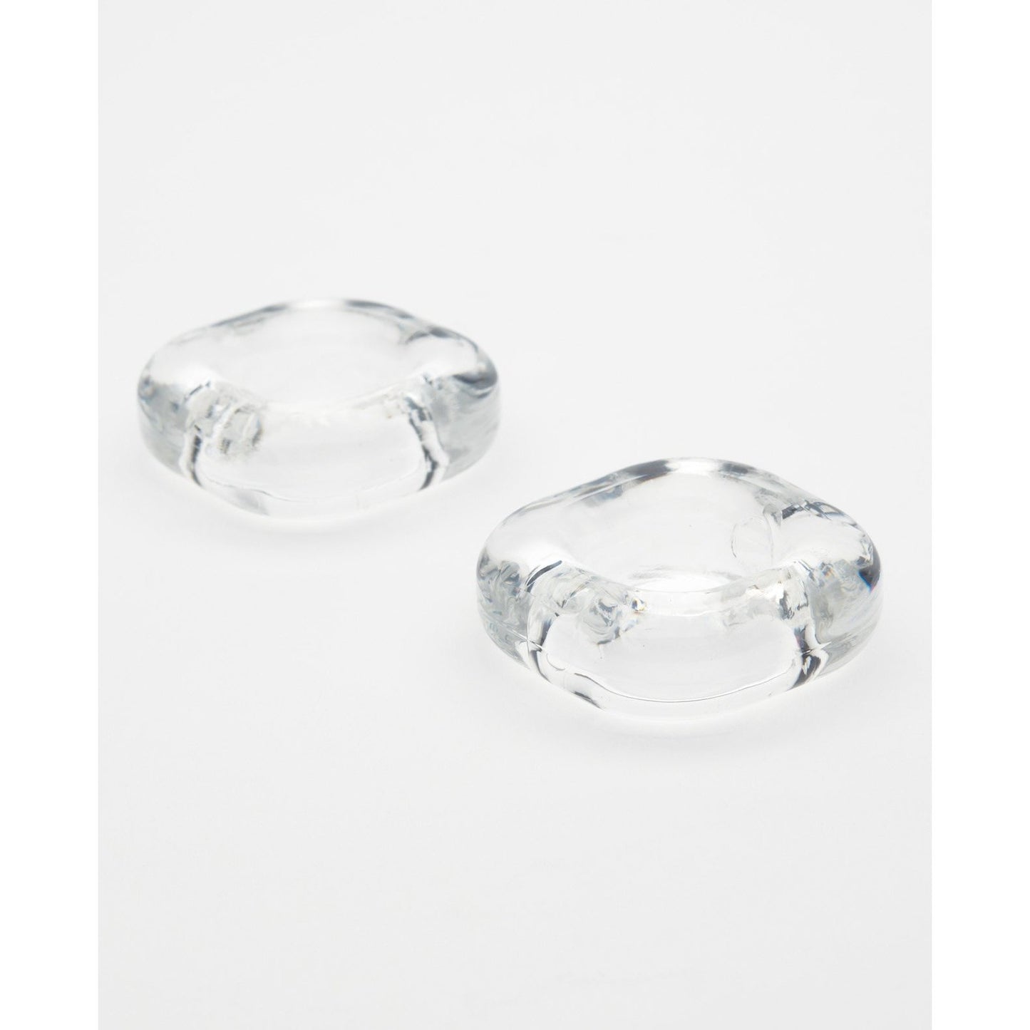 Two clear, rounded glass or acrylic objects are on a white surface. Their smooth curves and slightly concave centers resemble the sleek design of the Sport Fucker Boner Expansion Kit, with their transparent material subtly reflecting light to exude understated elegance.