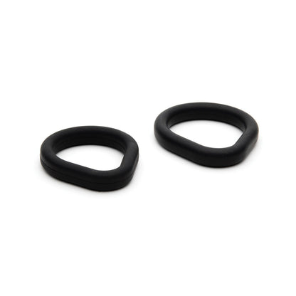 Two black rubber O-rings from the Sport Fucker Epic Hard on Kit by Sport Fucker are displayed on a white background. These silicone rings feature unique oval designs in different sizes, one slightly larger than the other, with smooth textures and rounded edges.