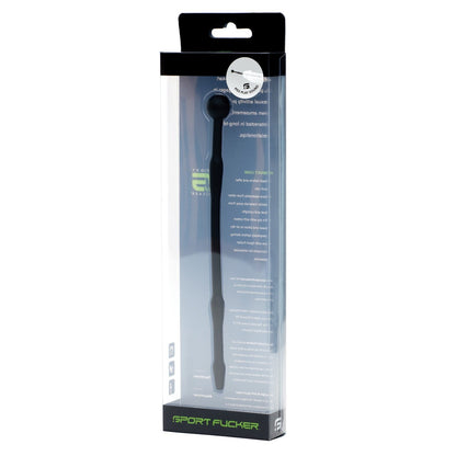 The image shows a Sport Fucker Piss Play Sound, a black silicone instrument, in a transparent plastic box. The mostly black packaging has white text and a small round sticker near the top. Made from medical-grade silicone, its labeled Sport Fucker at the bottom.