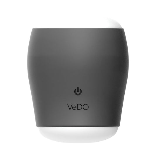 A two-toned cylindrical gadget with a dark gray exterior and white top, featuring a power button icon and the name VeDO on its front, is the VeDO Grip Rechargeable Vibrating Sleeve. Its sleek design with a silicone sleeve indicates it is a modern personal care product.